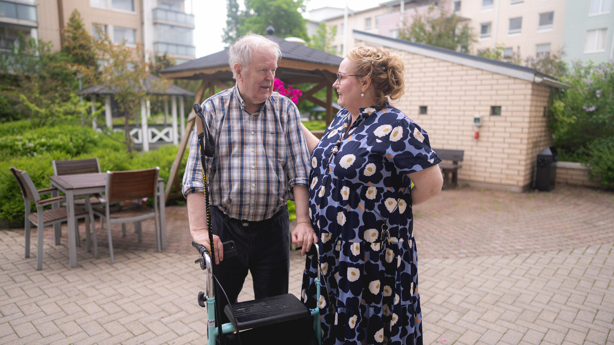 Iäkäs mies rollaattorin kanssa juttelee naisen kanssa pihalla